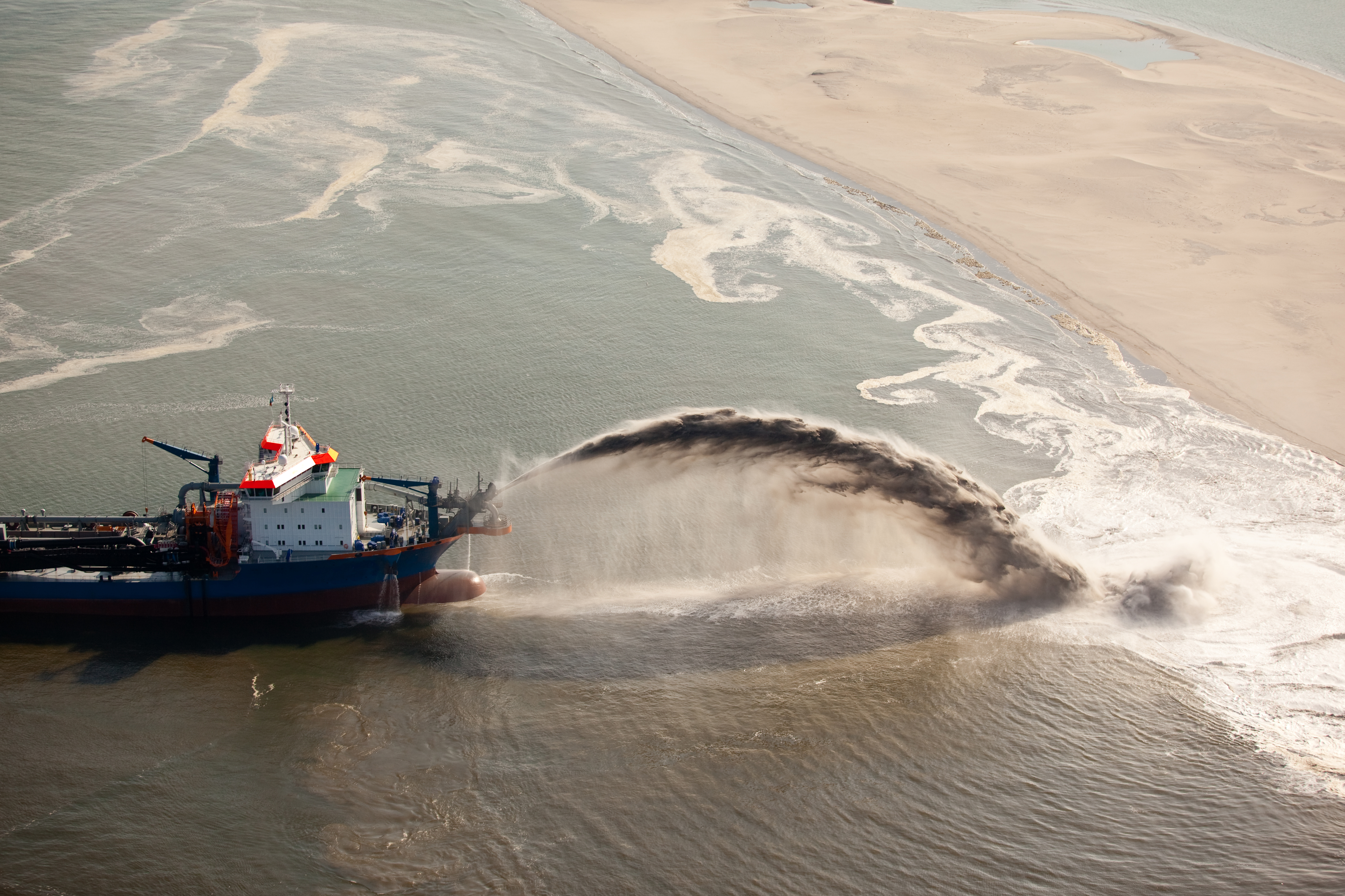 Hopper dredger rainbowing sand onto coastline
